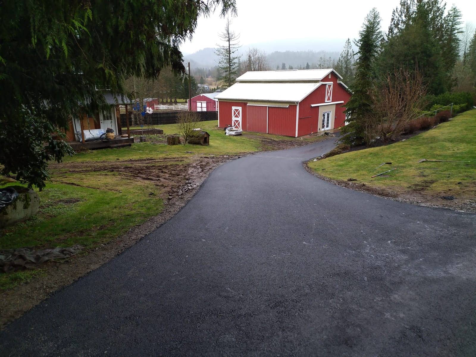 Fresh asphalt driveway curving past a red barn