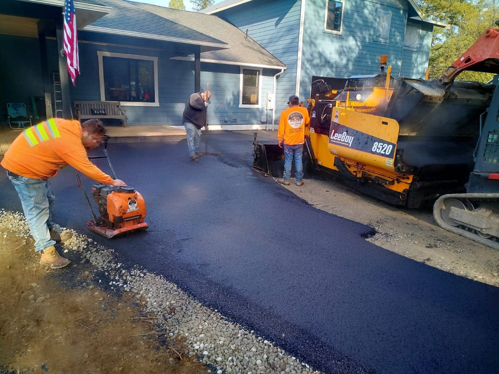 Crew rolling fresh asphalt on a new residential driveway