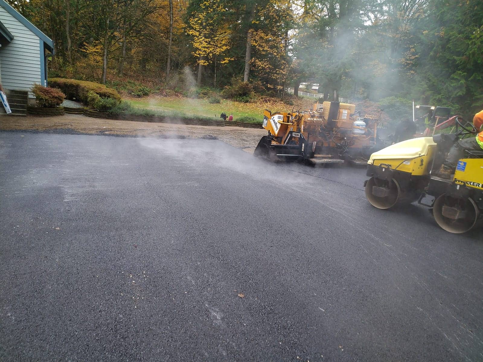 Steam rising off fresh asphalt as rollers compact a new surface