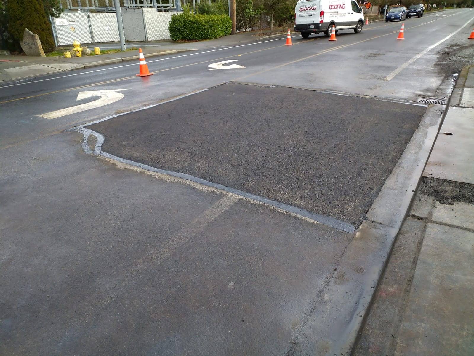 Completed asphalt street repair beside painted turn-lane markings, traffic cones alongside
