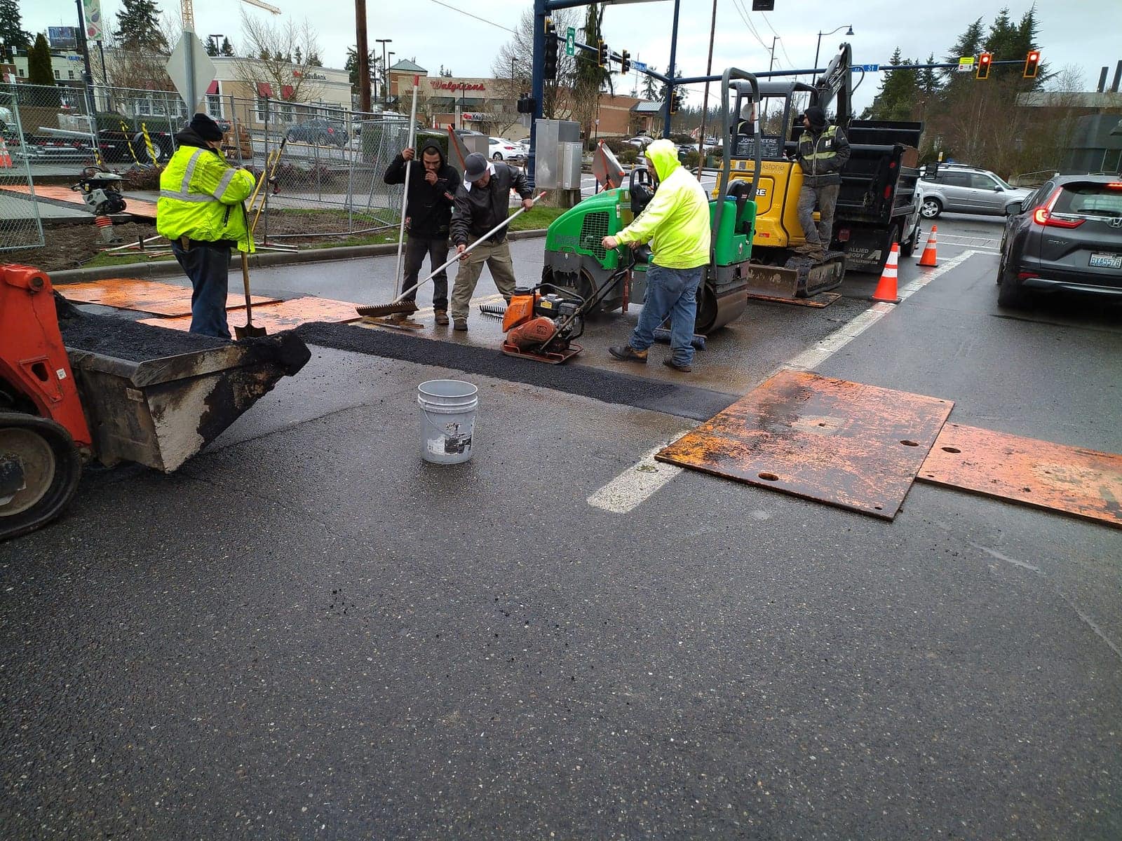 Crew compacting a fresh asphalt patch at a city intersection