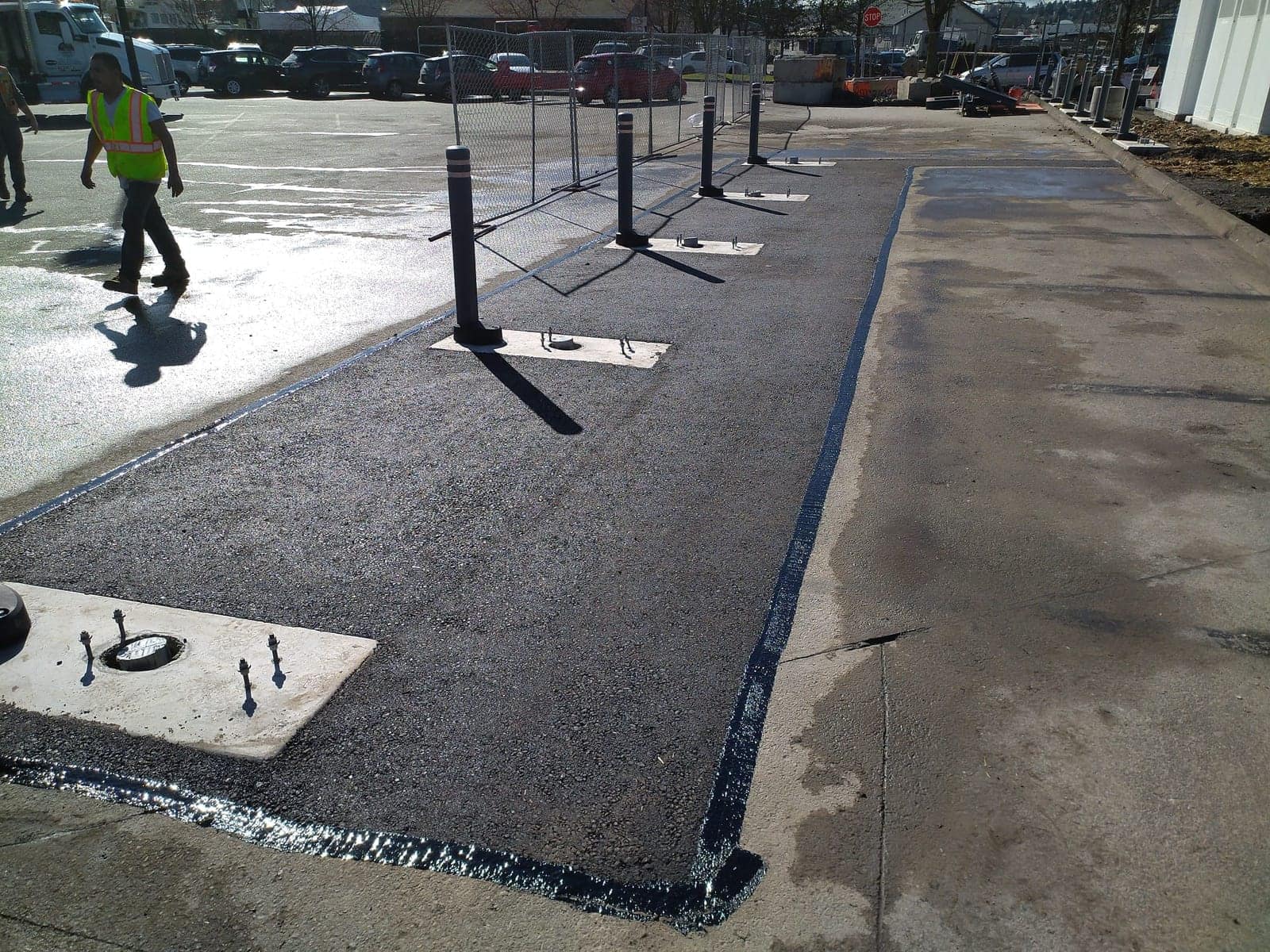 Fresh asphalt patch with tack-sealed edges along a commercial walkway