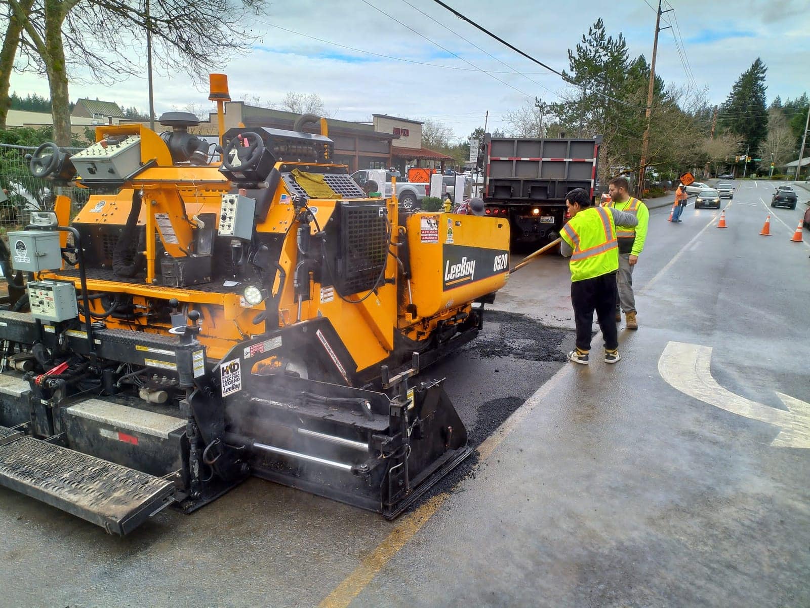 Paving crew laying fresh asphalt on a neighborhood street behind a dump truck