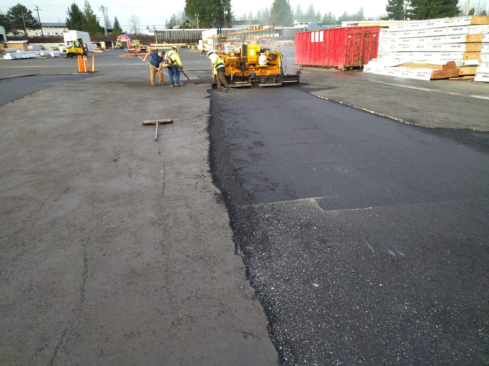 Fresh asphalt overlay meeting the older pavement it replaces across a commercial yard